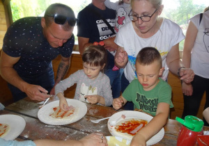 Dzieci przygotowują pizzę z pomocą rodziców.